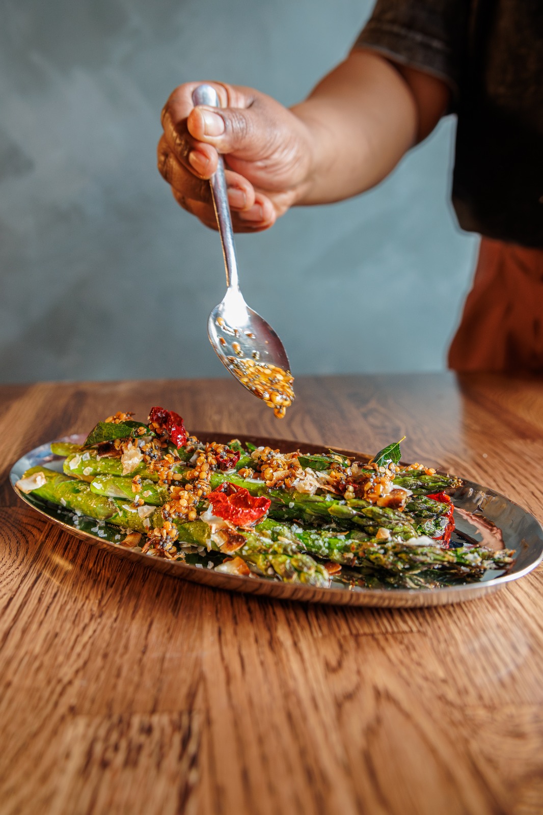 Fire-roasted asparagus poriyal being spooned with curry leaf coconut mustard tadka