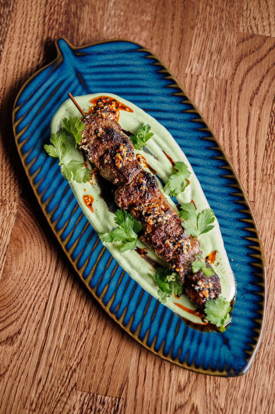 Uyghur Ribeye Kawap on a banana-leaf-shaped plate over garlic yogurt